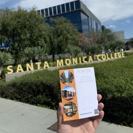 a hand holding up a porter mar vista flyer in front of a college monument sign