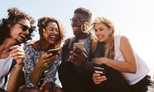 a group of friends sit outside laughing over their cell phones